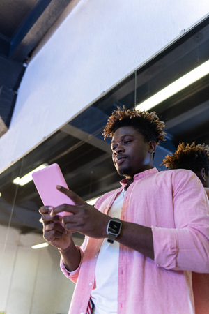 Concentrated young man. African American guy in pink shirt carrying pink smartphone and checking social mediaの写真素材