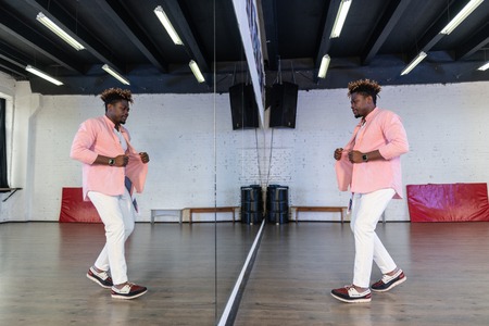 Festive outfit. Inspired flexible man in pink shirt standing in front of full length mirror and...