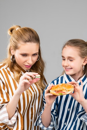 Comparing different sizes . Long-haired adult woman observing her tiny fake burger while little sister holding full-size versionの写真素材