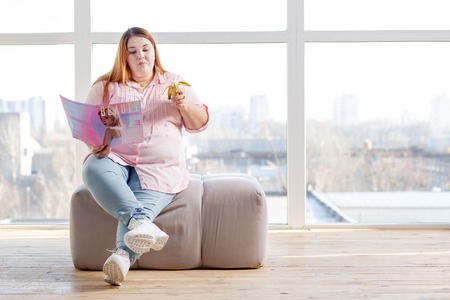 Nutritious banana. Nice good looking woman having a tasty snack while reading a fashion magazineの写真素材