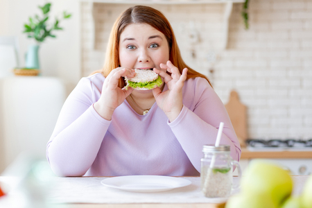 My meal. Hungry chubby woman looking at you while biting a tasty sandwichの写真素材