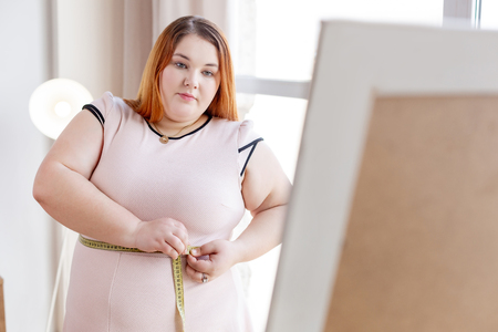 I am fat. Nice red haired woman measuring her waist while wanting to lose her weightの写真素材