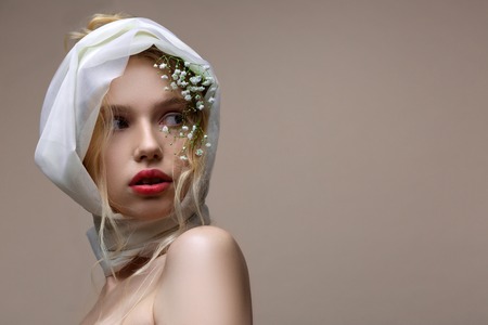 Silk scarf. Blue-eyed model with white silk scarf on her head and open shoulders posing near backgroundの写真素材