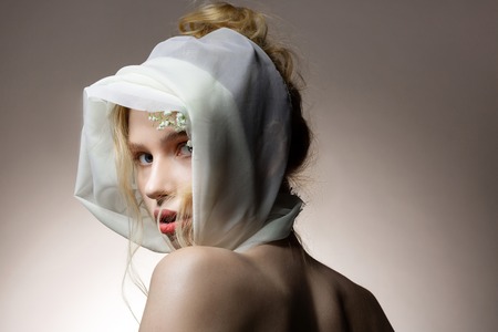 Scarf and flowers. Blue-eyed model with blonde wavy hair posing with silk white scarf and flowers on headの写真素材