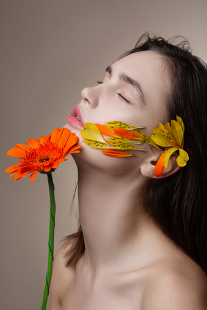 Tender model. Tender dark-haired model with petals on face and flower in hands closing eyesの写真素材