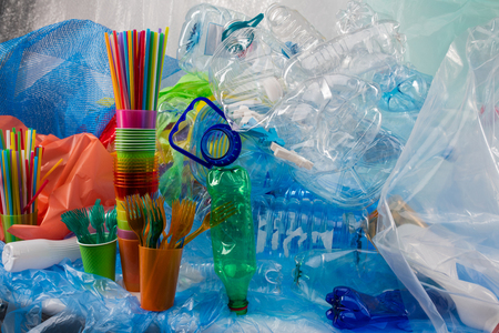 Bags and litters. Colorful plastic forks placed in plastic cup and standing near bunch of garbage as result of plastic captureの写真素材