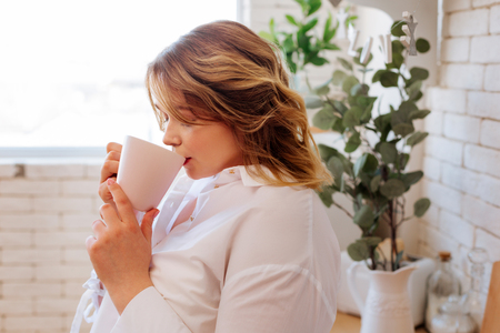 Black tea. Beautiful pretty woman holding a bog cup while drinking black tea at homeの写真素材