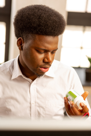 Is it helpful. Nice dark haired man holding a bottle with pills while deciding to take themの写真素材