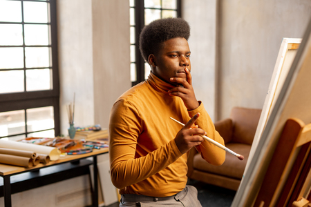 Being inspired. Creative young man looking at the canvas while thinking about what to paintの写真素材