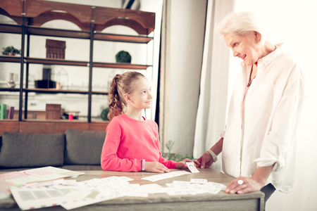 Girl listening. Cute smart dark-haired girl listening to granny attentively while studying lettersの写真素材