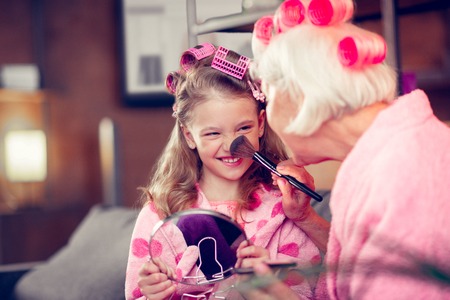 Brush on nose. Cute little girl smiling while doing makeup with granny having cosmetics brush on her noseの写真素材
