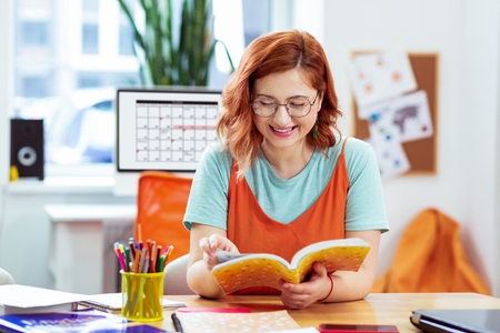 New information. Delighted young woman reading a book while learning new informationの写真素材