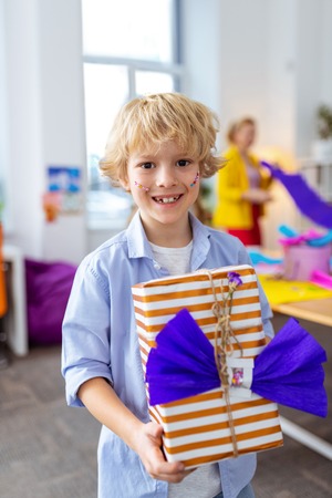 Smiling broadly. Cheerful boy smiling broadly after decorating big present box with nice bowの写真素材