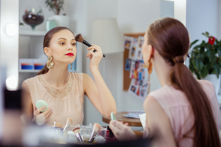 Natural tone. Serious attractive woman applying powder on her face while wanting to look naturalの写真素材