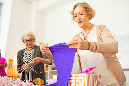 How to use it. Nice aged woman looking at the blue wrapping paper while thinking on how to use itの写真素材