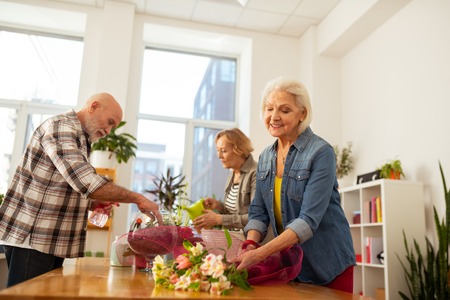 Bouquet design. Nice grey haired woman standing near flowers while creating the bouquet designの写真素材