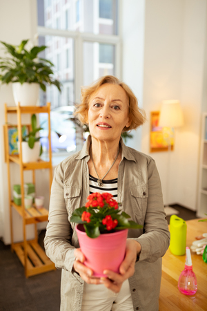 Nature lover. Nice good looking woman standing with a flower pot while smiling to youの写真素材