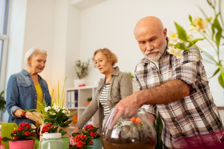 Potting idea. Nice good looking man looking at the transparent vase with ground while being engaged in workの写真素材