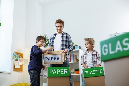 Concerned blonde boy. Ginger tall tutor working on sorting out different garbage while spending lessons with kidsの写真素材