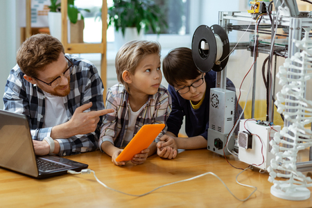 Connecting laptop. Attentive little engineers checking process of creating 3d-models while sitting...