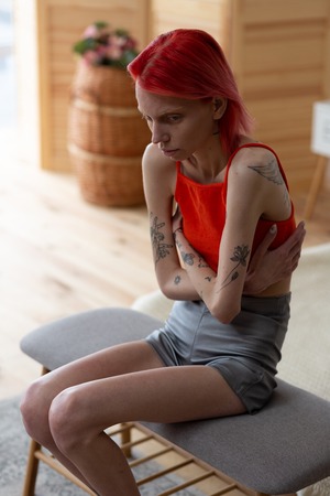 Shorts and top. Skinny tattooed red-haired woman wearing shorts and top having strong pain