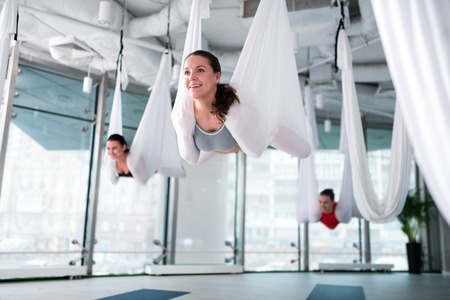 Aerial yoga pose. Dark-haired appealing woman feeling satisfied after successful aerial yoga pose