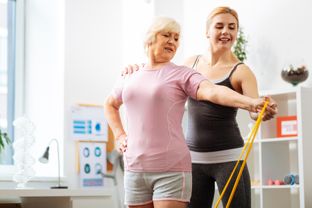 Professional help. Nice female coach standing behind her patient while helping her to do the exerciseの写真素材