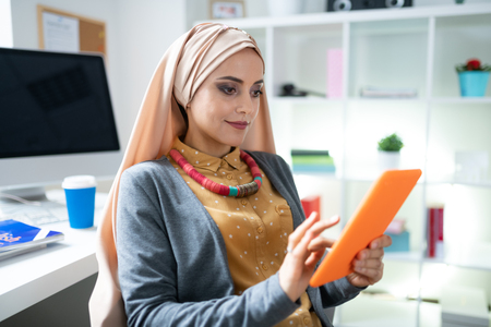 Nice makeup. Beautiful Muslim woman with nice makeup using her orange tablet reading electronic bookの写真素材