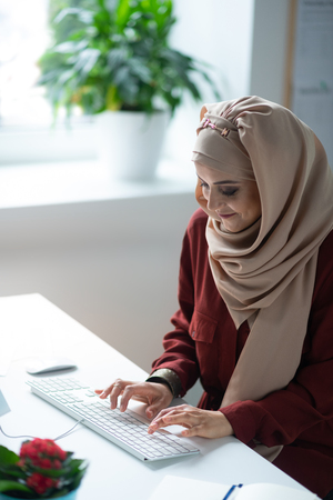 Woman smiling. Pleasant young Muslim woman smiling while working on computerの写真素材