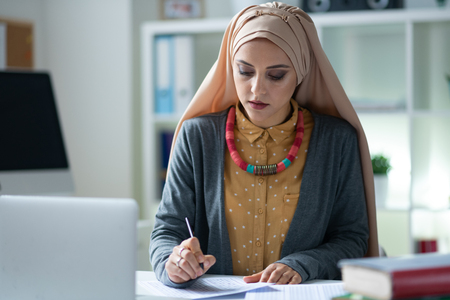 Teacher wearing hijab. Stylish Muslim teacher wearing hijab feeling busy correcting testsの写真素材