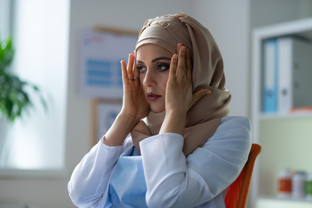 Chemist in hijab. Beautiful dark-eyed chemist wearing hijab and white uniform feeling unwellの写真素材