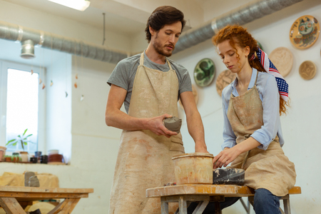 Master presenting clay. Concentrated professional couple working in equipped studio and holding fresh clayの写真素材