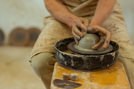 Manufacturing new pots. Qualified strong man with wet dirty hands producing on pottery wheel while staying in studioの写真素材