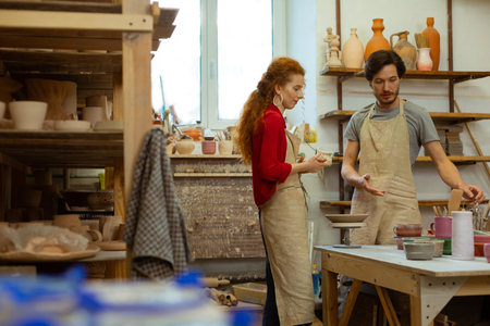 Pieces from clay. Pleasant good-looking couple staying in equipped studio and discussing steps in pottery artの写真素材