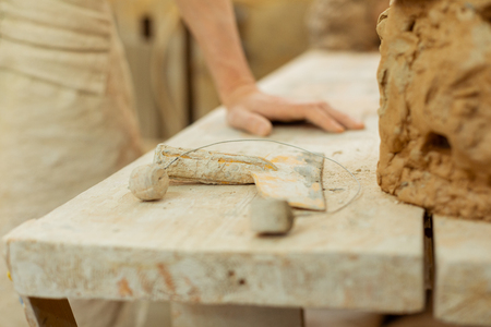 Intense working day. Man leaning on a working table covered in clay dirt and thinking on needed toolsの写真素材