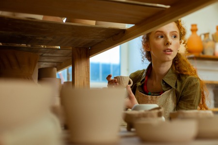 Checking finished figures. Curious long-haired curly girl looking out for inspiration while...