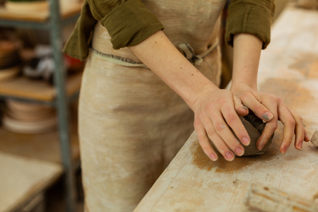 Starting new pot. Accurate woman in protective apron dealing with wet clay while working on a wooden surfaceの写真素材