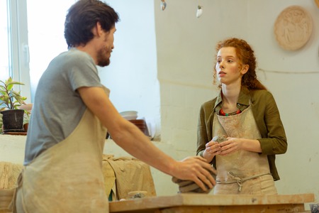 Dark-haired teacher. Impressed long-haired woman attentively listening to a professional pottery...