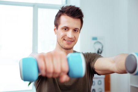 Training with dumbbells. Joyful nice man training with dumbbells while having a morning gymnastics