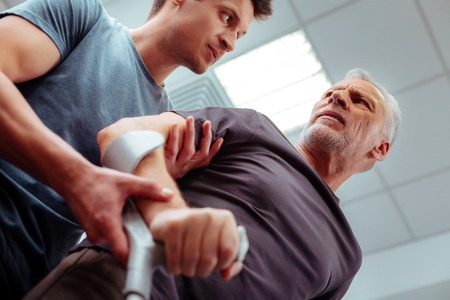 Professional assistance. Low angle of a male nurse looking at his patient while helping him to walkの写真素材