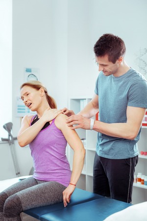 Unpleasant pain. Nice good looking woman sitting in front of her doctor while feeling pain in the shoulderの写真素材