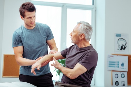 Young doctor. Handsome young man listening to his patient while holding his hand