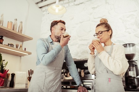 Enjoying the taste. Joyful handsome man and beautiful woman enjoying their fragrant coffee together.の写真素材