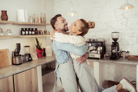 Life partners. Happy smiling couple joyously clasping in arms of each other in front of their kitchen equipment.の写真素材