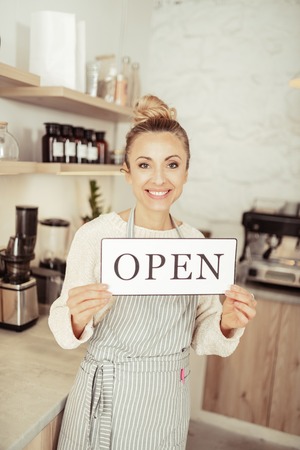 We are opened. Beautiful smiling startup owner greeting guests of her new cafe.の写真素材