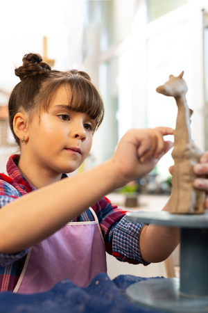 Modeling clay giraffe. Talented dark-eyed beautiful girl modeling clay giraffe at the art lessonの写真素材