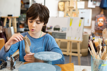 Modeling figures. Funny cute handsome boy feeling excited while modeling figures out of clayの写真素材