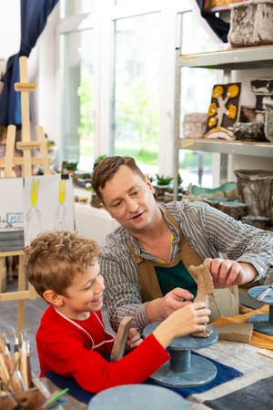 Modeling with teacher. Talented cute boy smiling while modeling clay figures with his teacherの写真素材