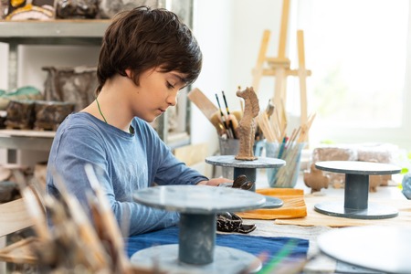 Sitting and modeling. Dark-haired boy sitting near the window and modeling polymer clay figuresの写真素材
