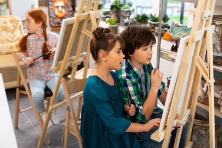 Children feeling excited. Active talented good-looking children feeling excited while drawing in art schoolの写真素材